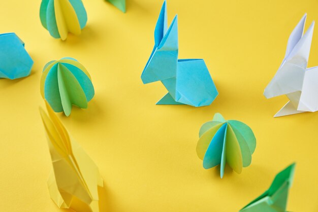 Paper origami Esater rabbits and colored eggs on yellow wall. Easter celebration concept