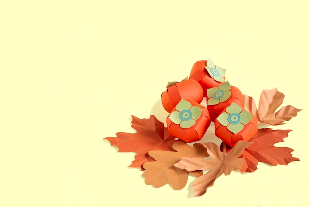 Paper persimmon and autumn leaves on yellow background