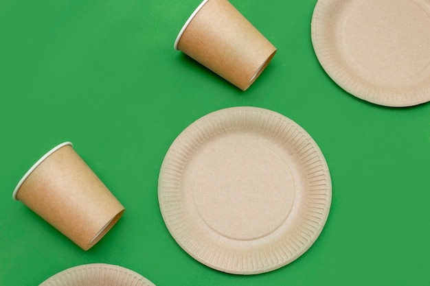 Piatto di carta, vetro su sfondo verde. piatti ecologici, compostabili, materiali usa e getta e riciclabili. zero plastica, salviamo il pianeta, basta plastica. il concetto di riciclaggio dei rifiuti