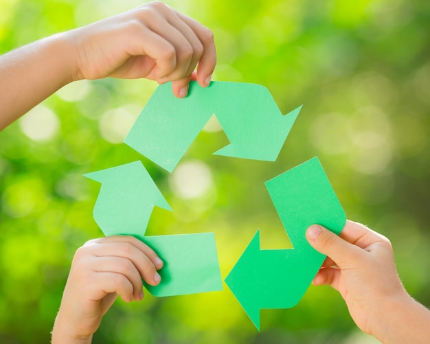 Paper RECYCLE sign in childrens hands against green spring background Earth day concept