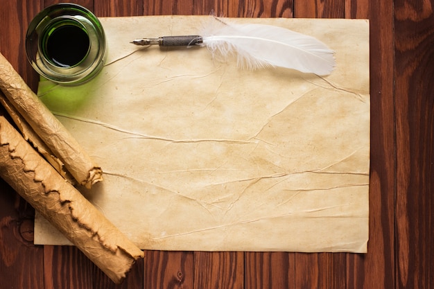 Paper scroll with feather pen and ink pot on wood background