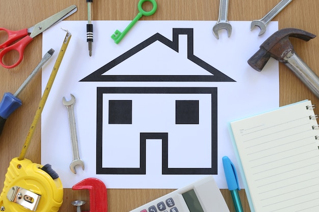 Paper shaped house on a background of brown wood and Craftsman tool.