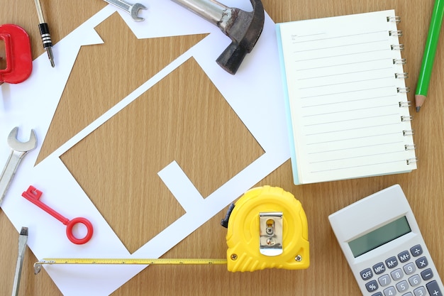 Paper shaped house on a background of brown wood and Craftsman tool.