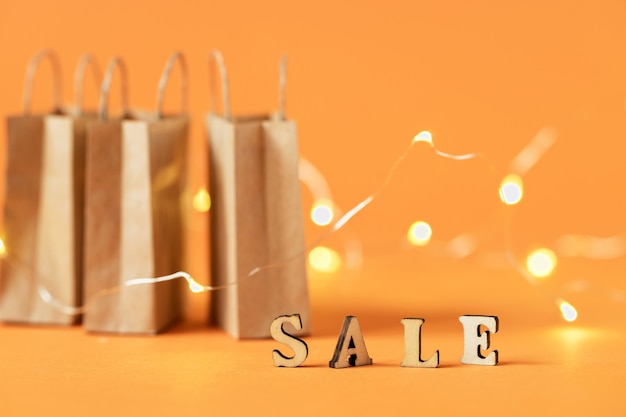 A paper shopping bag on an orange background. The concept of delivery of purchases and sales. The word sale. Glare in the background.