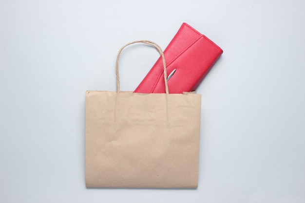 Paper shopping bag, red leather wallet on gray table. Top view