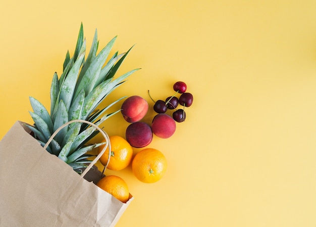 Paper shopping bag with assorted fruit coming out of the bag on yellow background. Copy space. Top view.