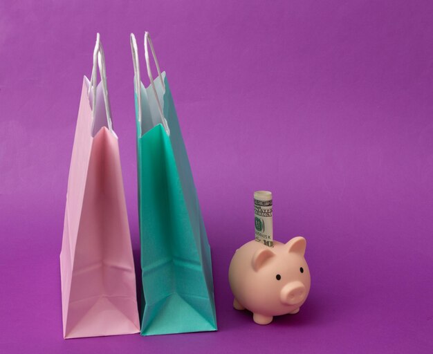 Photo paper shopping bags and piggy bank on purple background save money shopping concept