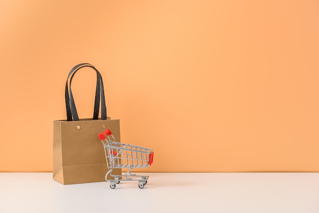 Paper shopping bags and shopping cart or trolley on white table and pastel orange