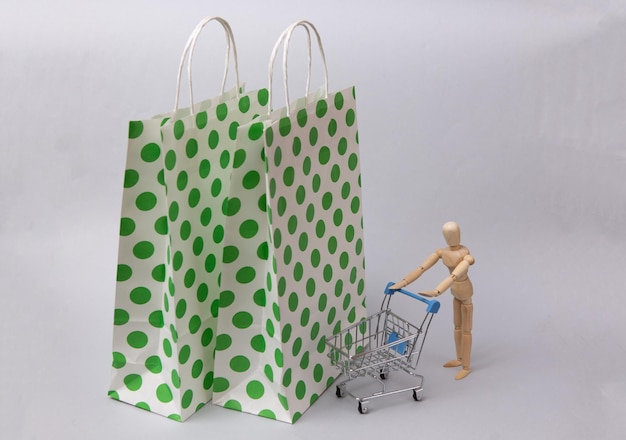 Paper shopping bags and wooden puppet with shopping cart on white background