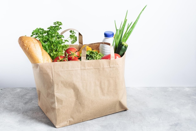 Paper shopping box full of fresh organic vegetables and grocery products on grey table