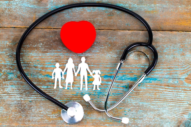 Бумажный силуэт семьи, стетоскоп и сердце на деревянном фоне. Концепция медицинского страхования.