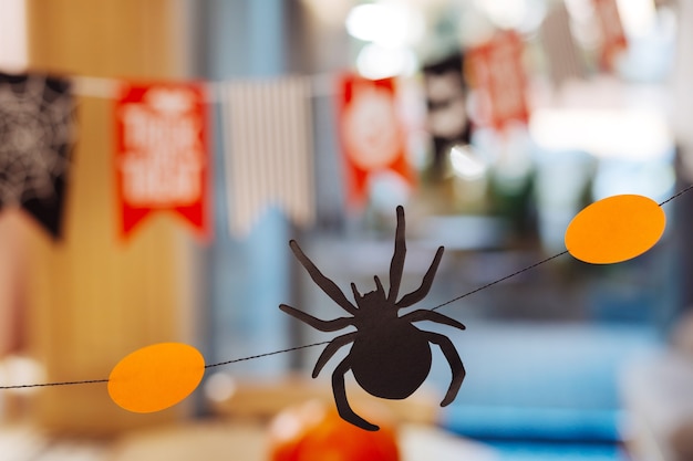 紙蜘蛛。素晴らしいハロウィーンパーティーのためのオレンジ色の装飾の間に横たわっている小さな怖い紙のクモのクローズアップ
