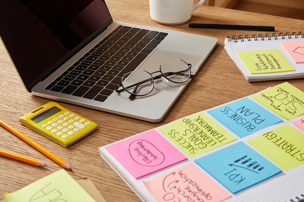 Paper stickers with business strategy, calculator and laptop on tabletop