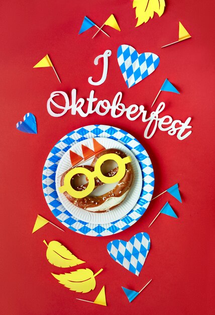 Paper text "I love Oktoberfest", pretzel and matching decorations on dark red paper