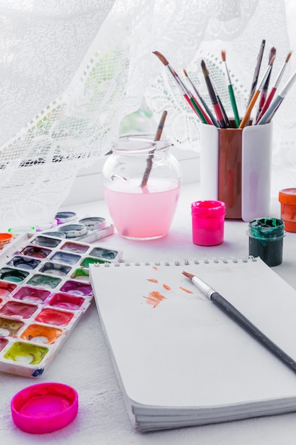 Paper, watercolors, paint brush and some art stuff on wooden table 