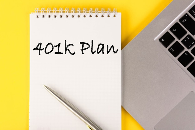 Paper with a 401k plan on the table with a laptop on a yellow wall.