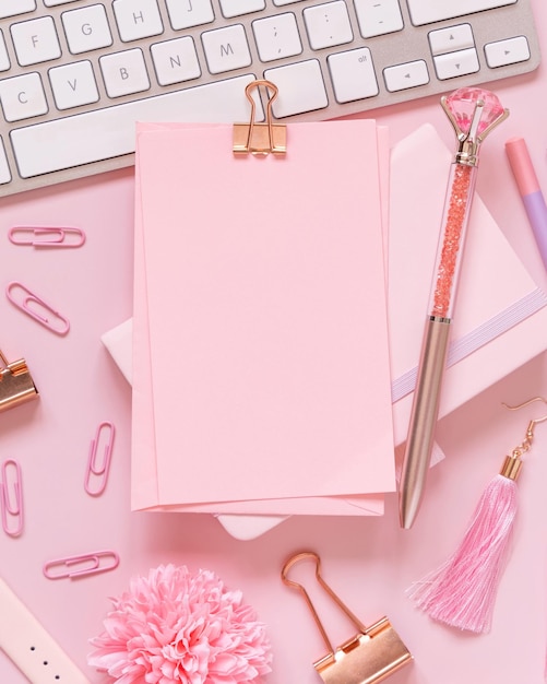 Photo paper with a clip pink girly accessories and keyboard on pastel pink top view mockup