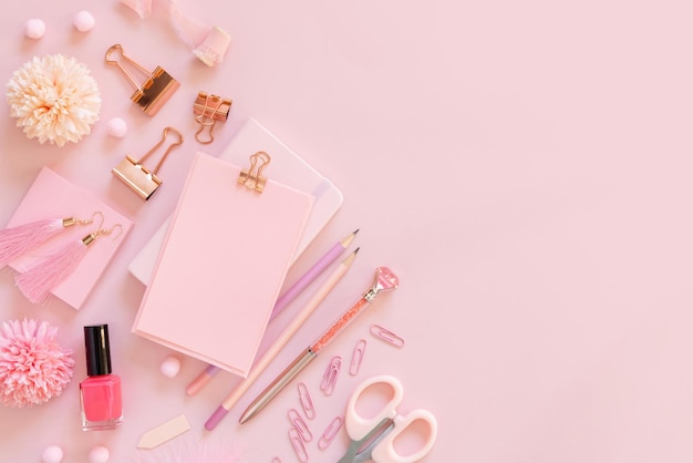 Carta con una clip e accessori per la scuola rosa su mockup rosa pastello con vista dall'alto luogo di lavoro femminile con forbici, matite, penna, graffette, orecchini e smalto, concetto di ritorno a scuola