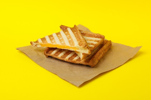 Paper with grilled sandwiches on yellow background