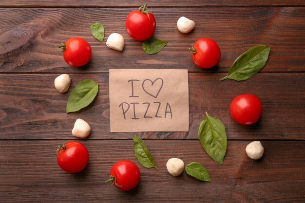 Paper with text I LOVE PIZZA and ingredients on wooden table