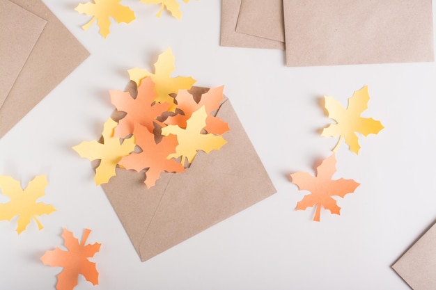 Paper yellow and orange maple leaves in a craft envelope on a pink background Top view