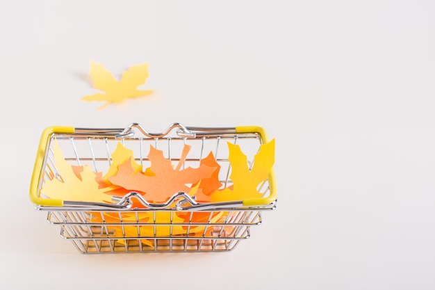 탁자 위의 쇼핑 바구니에 종이 노란색과 주황색 단풍나무 잎