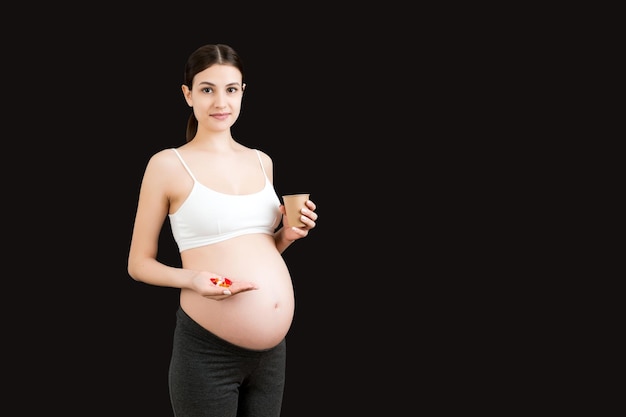 Papieren beker en een hoop pillen in de handen van de zwangere vrouw op een kleurrijke achtergrond met kopieerruimte Gezondheidszorgconcept