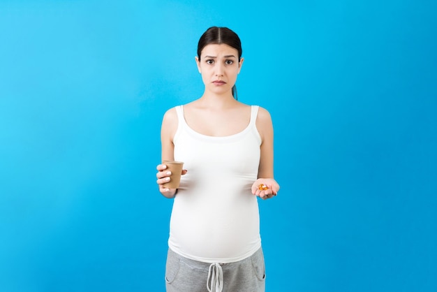papieren beker en een hoop pillen in de handen van een zwangere vrouw op een kleurrijke achtergrond met kopieerruimte gezondheidszorgconcept