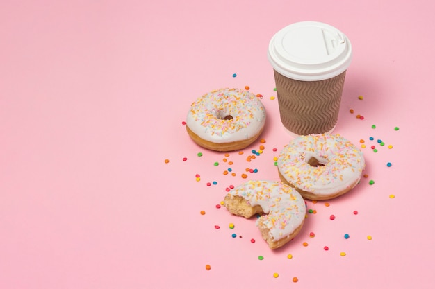 Papieren beker met koffie of thee, verse smakelijke zoete donuts op een roze achtergrond. Fast-food concept, bakkerij, ontbijt, snoep, koffieshop. kopie ruimte.