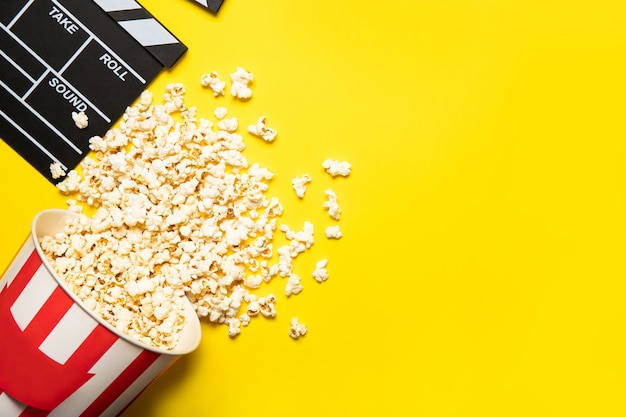 Papieren beker met popcorn en filmklep op een gele achtergrond, plaats voor tekst