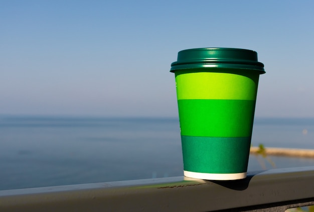 Papieren beker met thee, koffiedrank op een glazen tafel behoort tot de achtergrondplant en een groene muur. zero west-concept.