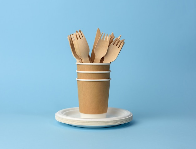 Papieren beker, witte borden en houten vorken en messen op een blauwe achtergrond. plastic afkeuringsconcept, geen afval