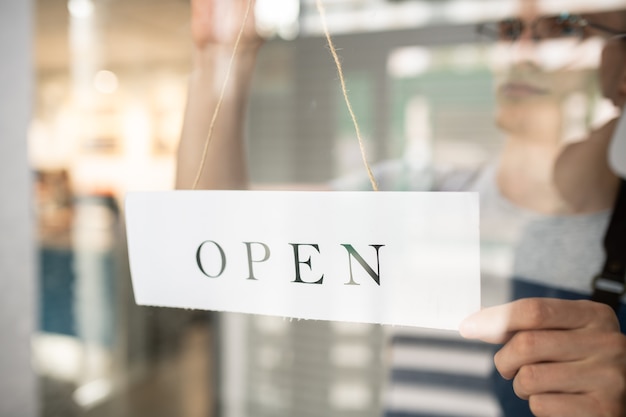 Foto papieren bericht met de tekst open gehouden door ober of barista achter transparante deur van cafetaria