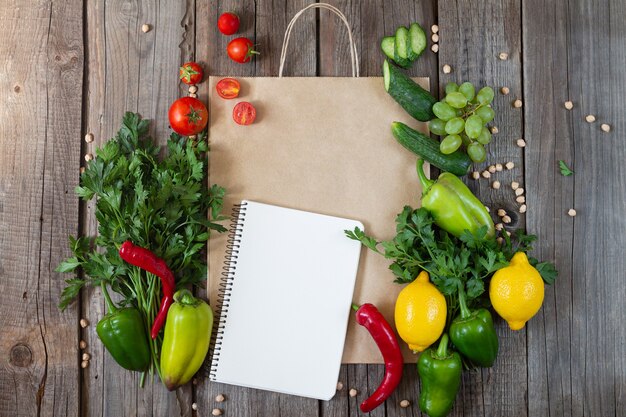 Papieren boodschappentas met lege notebook en verse groenten en fruit op houten tafel