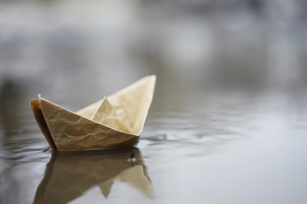 Foto papieren boot in het water op straat. het concept van de vroege lente. smeltende sneeuw en een origamiboot op watergolven.