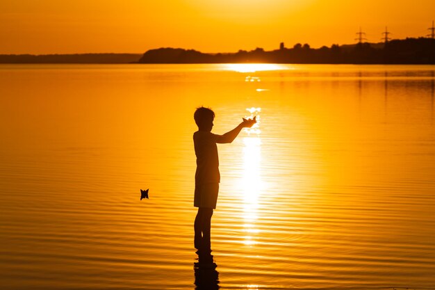 Papieren boot is in de handen van een kind Mooie oranje zonsondergang Origami Silhuette tegen zonsondergang Zomerroeping concept