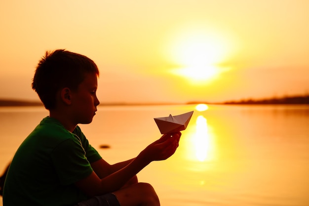 Papieren boot is in de handen van een kind Mooie zomerse zonsondergang Origami