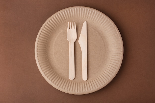 Papieren bord met een vork en mes, milieuvriendelijk afval, op een bruine achtergrond