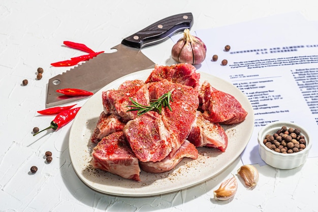 Papieren culinair recept voor de bereiding van varkensvlees. Ruwe ingrediënten omvatten stukjes varkenslende, specerijen en kruiden. Voorbereiding gezonde voeding concept hard licht donkere schaduw witte achtergrond close-up