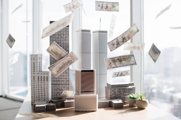 Papieren dollars honderd bankbiljetten vallen op architectonisch schaalkartonmodel van gebouwencomplex