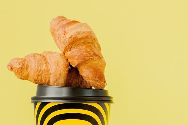 Papieren kopje koffie en croissants op een geel.