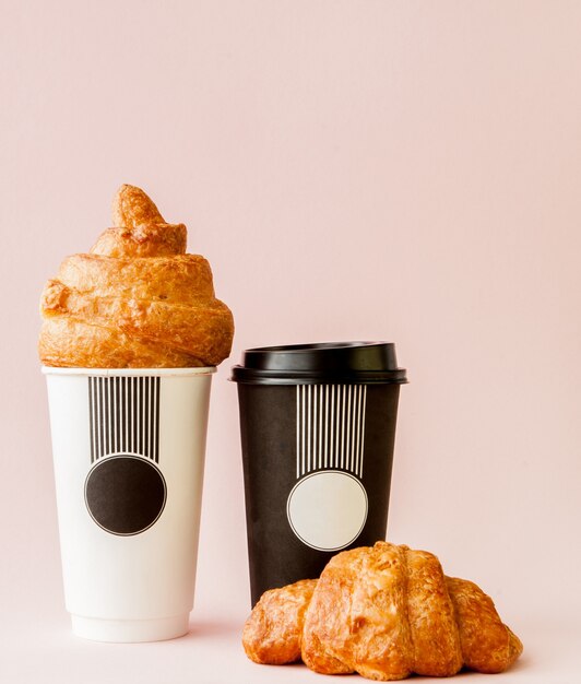 Papieren kopje koffie en croissants op een roze muur, kopieer ruimte.