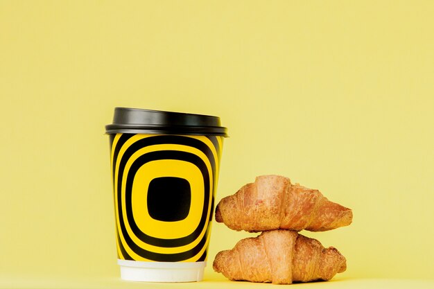 Papieren kopje koffie en croissants op geel