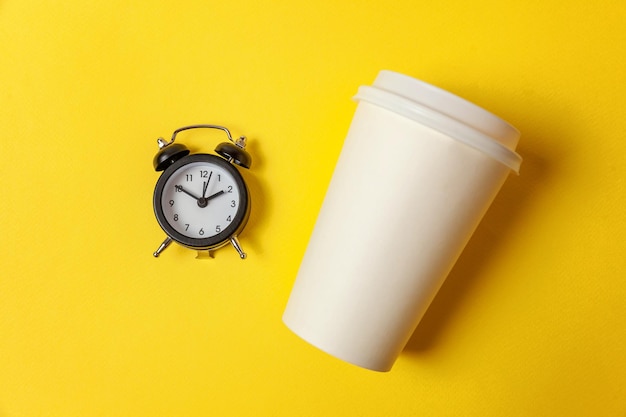 Papieren kopje koffie en wekker op gele achtergrond