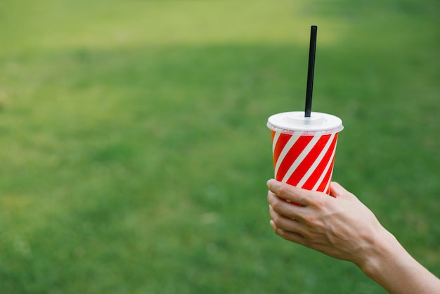 Papieren wegwerpglas met een stro rode en witte streep voor drankjes in de handen van een vrouw