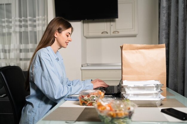 papieren zak en wegwerp-takeaway voedselcontainers op de tafel jonge vrouw die gezond voedsel bestelt van een laptop Takeaway voedsel thuislevering lunch