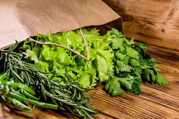 Papieren zak met sla, rozemarijn en peterselie op een houten tafel Veganistisch eten