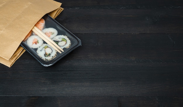 Papieren zak sushi lade op zwarte houten tafel. Voedsel concept.