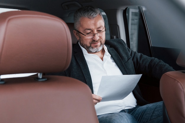 Papierwerk op de achterbank van de auto. Senior zakenman met documenten