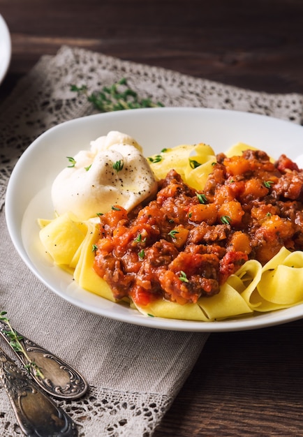 Паста Паппарделле с мясным рагу и сыром буррата на деревенской деревянной поверхности. Итальянская кухня. Выборочный фокус.